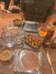 Amy enjoys a meal at a table in a restaurant, with a plate of food in front of her.