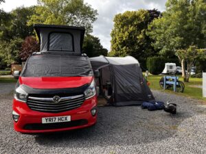  Chris' red campervan parked with a tent set up on top, ready for an outdoor adventure with family.