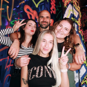 Amy and three of her ostomate friends smiling for a photo in front of colorful graffiti art on a wall.