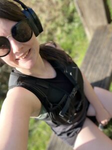 Amy, wearing sunglasses and a running vest relaxes on a bench, looking content in her casual setting.