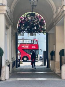 A red double-decker bus parked in front of a large stone archway in Paris.