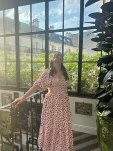 Amy, in a red dress, stands on a balcony, looking out at the view showing that travelling with a stoma is possible!
