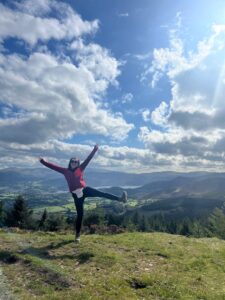 Amy pulls a silly pose on top of a mountain with lovely, scenic views, empowering others to do anything with a stoma.