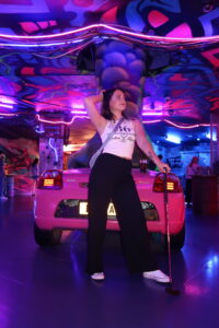 Amy strikes a pose at mini golf, holding her golf club and bright lights behind her.