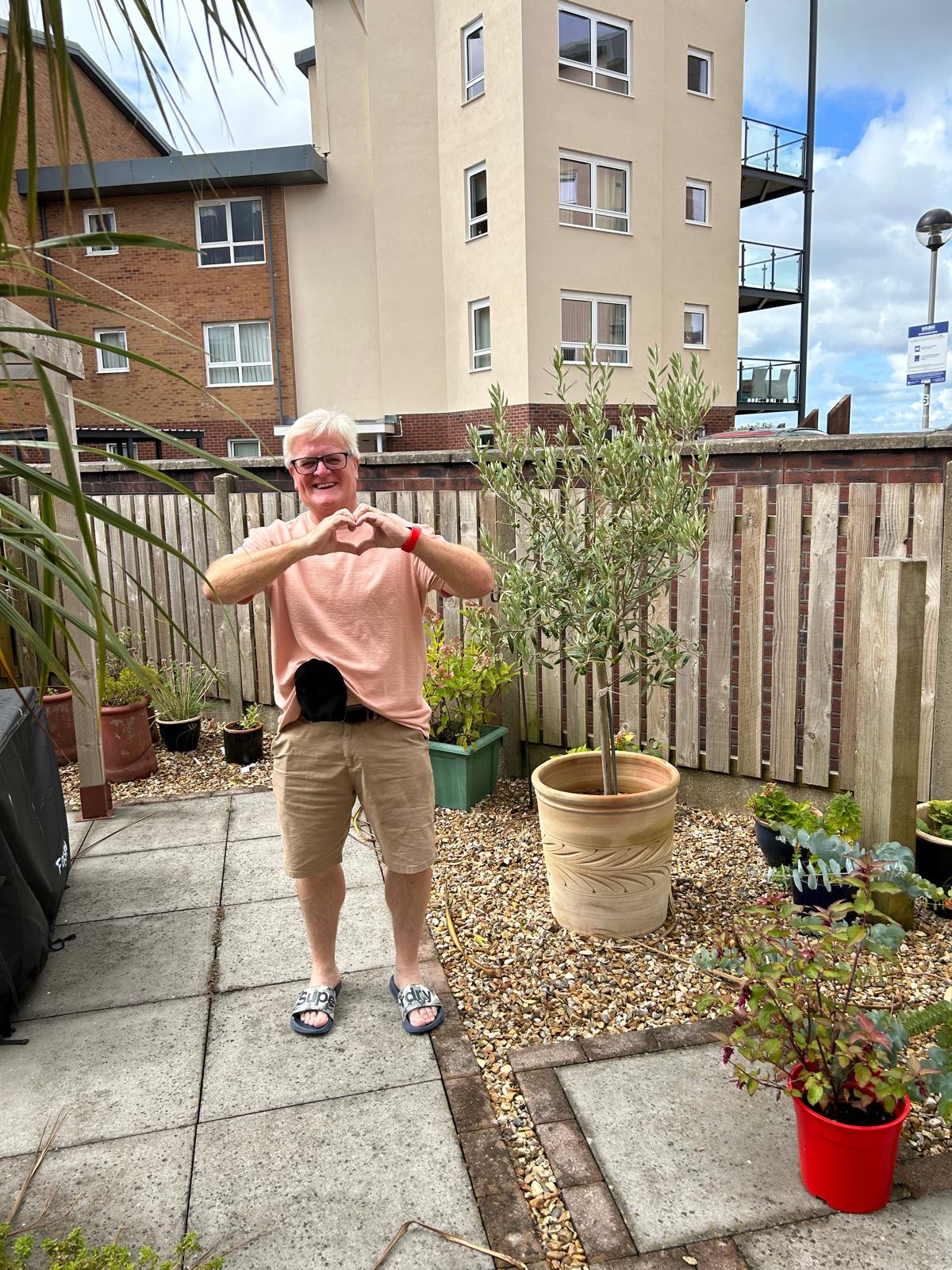 A man standing in a garden making a heart-shape with his hands